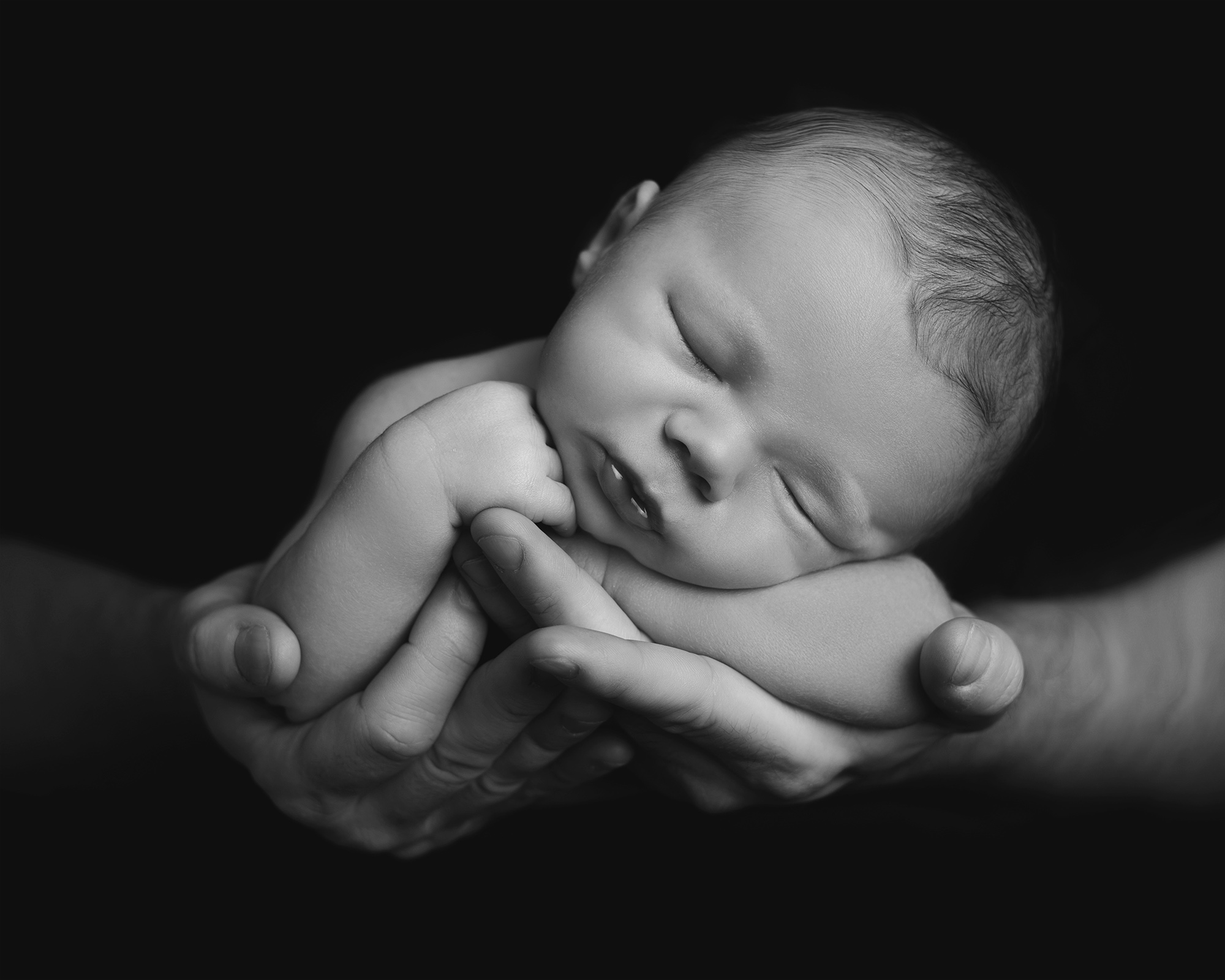baby being held in parents arms with a black background by newborn photographer in Guildford, Surrey