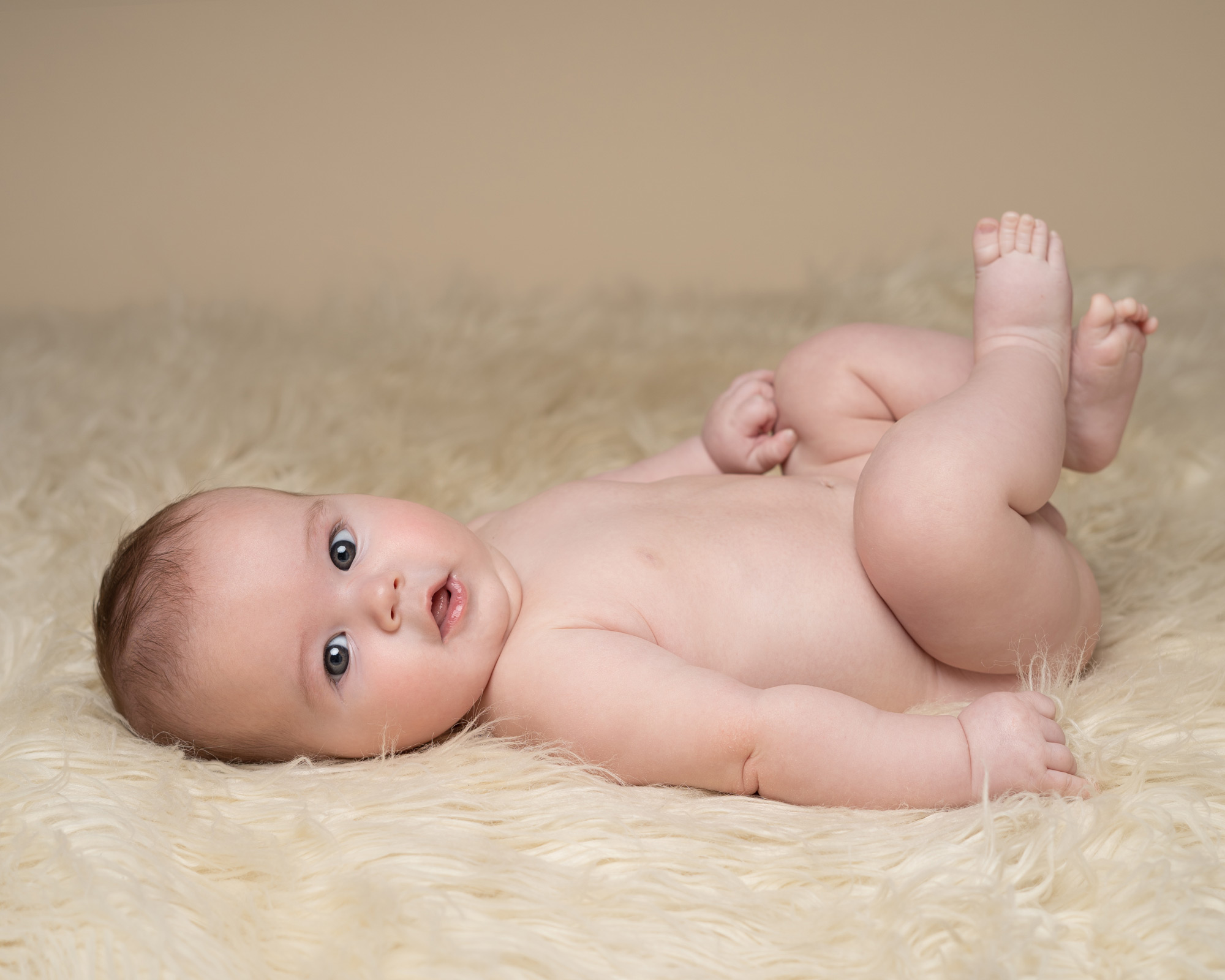 baby lying down on fur blanket by BABY & FAMILY PHOTOGRAPHER IN SURREY