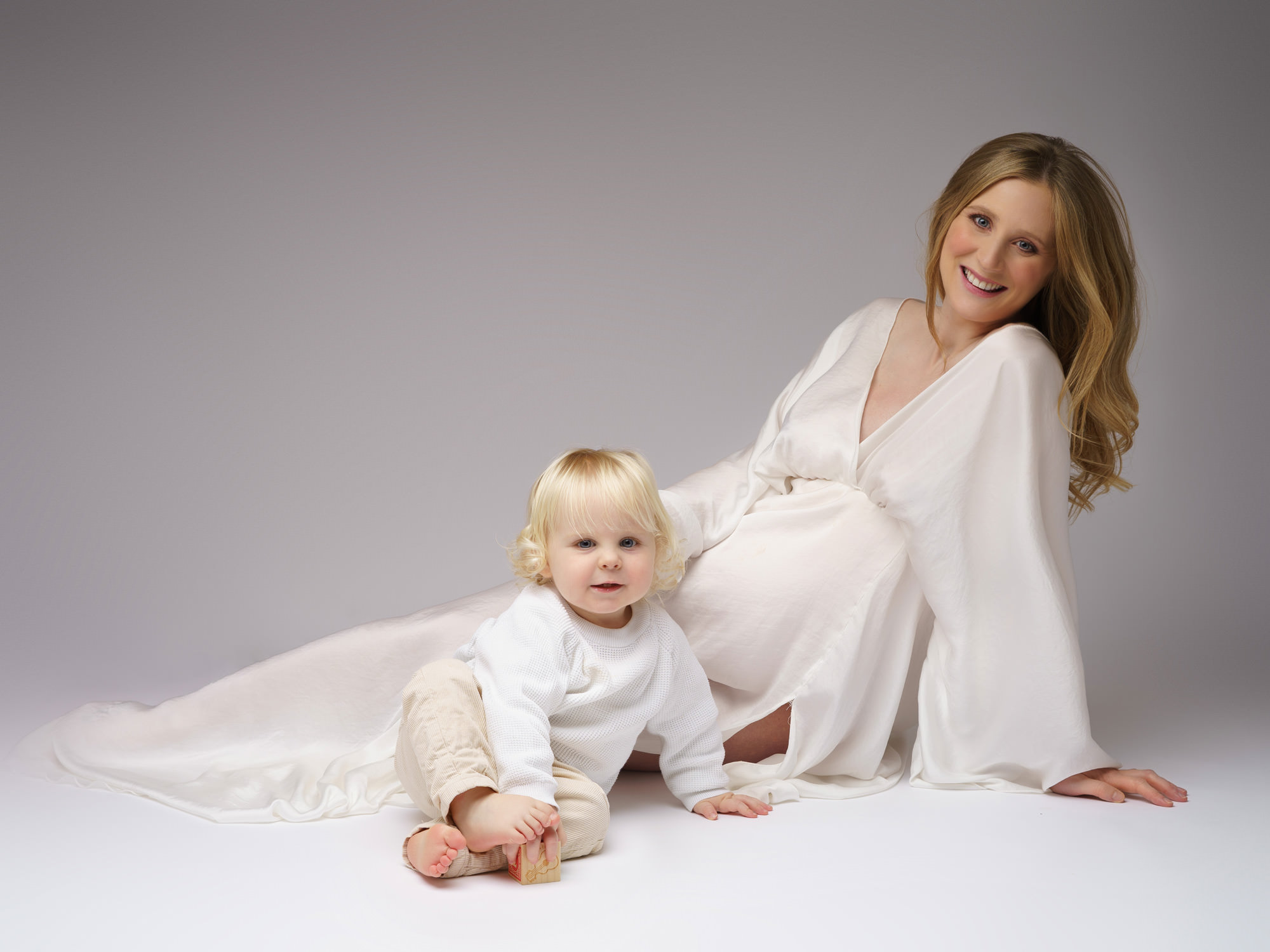 Pregnant mum wearing white dress with her toddler with blonde hair by maternity photographer in Surrey