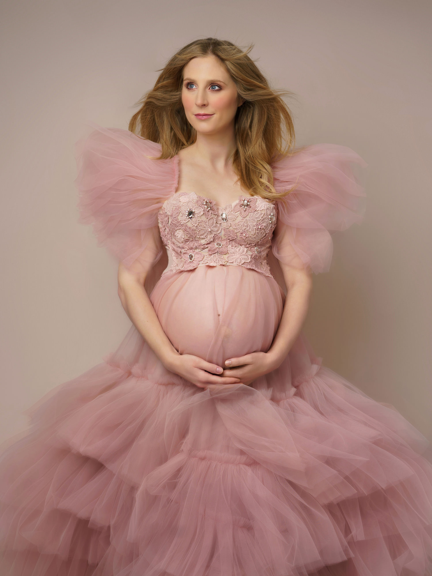 pregnant woman in pink frilly dress with hands under her baby bump by maternity photographer in Surrey